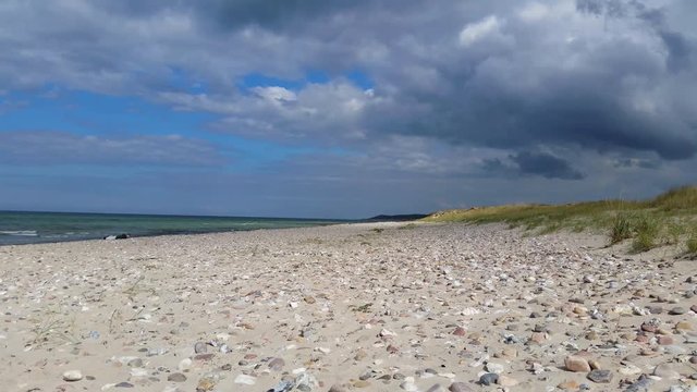 Liseleje Beach by the Tisvilde forest and coastal area on the Danish island of Zealand. Sunny beach with dramatic clouds coming in. Change of weather. Scattered stones. A person resting by the water.