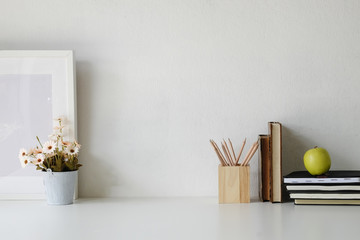 Obraz na płótnie Canvas Workspace flower pot, pencil, books and photo frame on white table.
