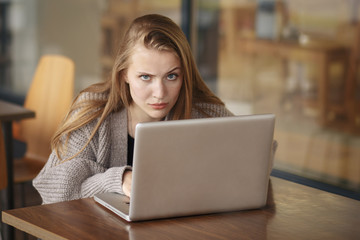 Young woman in sitting at desk with laptop staring at camera