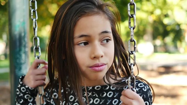 Eleven-year-old girl with attitude bullies someone out of frame on a swing-set
