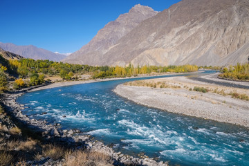 Blue water of winding Gilgit river of Indus flowing through Gupis, Ghizer with mountains and autumn forest. Gilgit Baltistan, Pakistan.