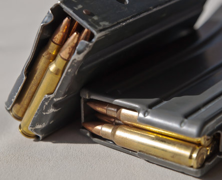 Two metal rifle magazines, one stacked upon the other, loaded with .223 caliber bullets