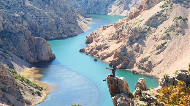Male sitting alone on the edge of rock in the middle of Zrmanja canyon with wide open hands.