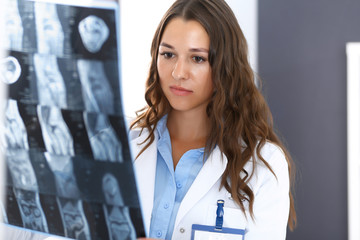 Doctor woman examining x-ray picture while standing near window in hospital. Surgeon or orthopedist...