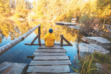 A man sits on a wooden pier over the lake in autumn and looks at the water