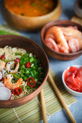 Asian food, Tom Yam and Ramen with shrimps, Thai food in wooden bowl, Egg noodles, Preparation, Chilli peppers, onion and mushrooms, Spicy, Lght gray background, Closeup, Selective focus