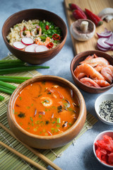 Asian food, Tom Yam and Ramen with shrimps, Thai food in wooden bowl, Egg noodles, Preparation, Chilli peppers, onion and mushrooms, Spicy, Lght gray background, Closeup, Selective focus