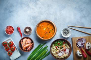 Fototapeta na wymiar Asian food, Tom Yam and Ramen with shrimps, Thai food in wooden bowl, Egg noodles, Preparation, Chilli peppers, onion and mushrooms, Spicy, Top view on light gray background, Selective focus