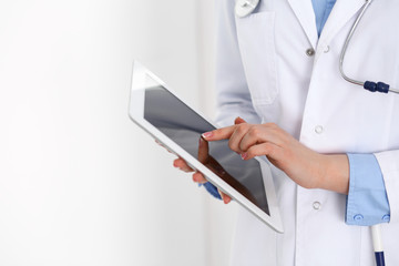 Woman doctor using tablet computer while standing straight in hospital closeup. Healthcare,...