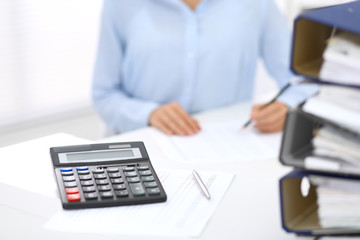 Calculator and binders with papers are waiting to be processed by business woman or bookkeeper back...
