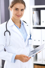 Doctor woman in clinic office. Female physician at work using digital tablet  while standing straight at hospital. Medicine and healthcare concept