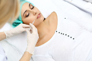 Professional cosmetologist making injection in face, lips. Young woman gets syringe with filler for face contouring or augmentation. Face aging, rejuvenation and hydration procedures