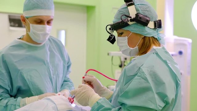 woman surgeon and her male assistant are working over nose and nasal septum of patient