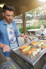 Man cooking skewers on grill for party
