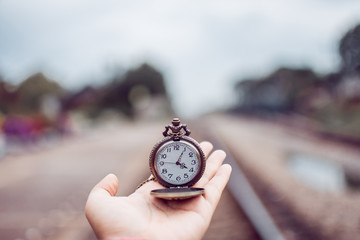hand holding vintage clock on hand at rail train. subject is blurred.