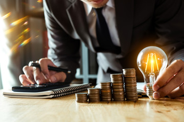 businessman holding coins putting in glass with using smartphone and calculator to calculate ...