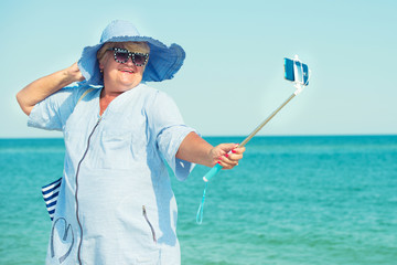 An elderly woman in a hat rest on the sea and making photo against the background of the sea. Summer vacation