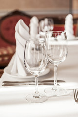 Two empty wine glasses on a served table. White tablecloth, glasses, plates, appliances, red furniture