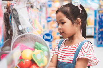Cute asian child girl choosing the toy and shopping in supermarket