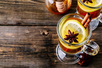 Hot spiced Apple cider Toddy with lemon, honey and cinnamon stick in glass on wooden background