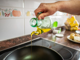 Hand holding bottle dropping olive oil in pan. Cooking concept in kitchen home made