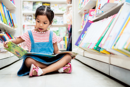 Cute Asian Child Girl Select Book And Reading A Book In Bookstore In Supermarket