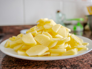 Pile of laminated potatoes on white plate with other ingredients on background. Spanish omelet recipe