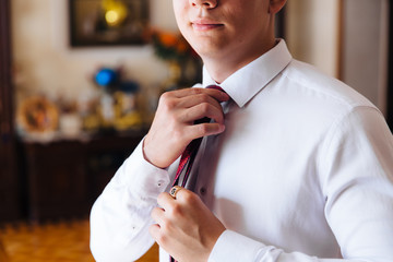 Close-up of a cropped frame of a slender business man in a trendy suit wearing dark trousers and a white shirt is holding a tie in his hands. A businessman is going to try on a red tie.