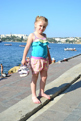 girl standing barefoot on the shore against the sea landscape holding sandals in her hand 