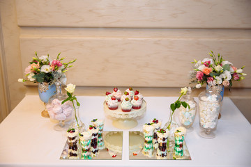 Candy bar, a table with sweets and desserts on the table. Buffet with delicious cupcakes, cake pops, biscuits, flowers.