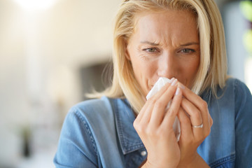 Middle-aged woman with allergy blowing her nose