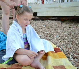 girl sitting wrapped in a towel after bathing on the beach  