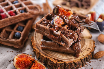 Delicious waffles with fig slices and chocolate sauce on wooden board