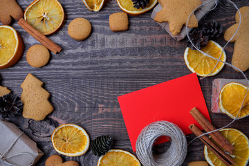 Fototapeta na wymiar Christmas top view over a brown wooden background with gift boxes packed in a craft paper with dryed oranges, cookies and christmas decorations. Flat lay, copy space, holiday banner.