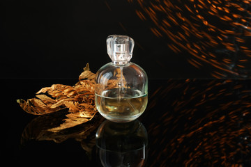 Bottle of perfume with golden leaves and sparkling on dark background