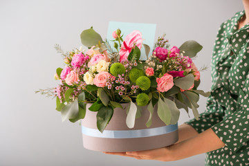 Woman holding gift box with beautiful flowers on light background