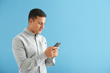 Young man with mobile phone on color background