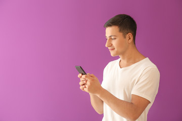 Young man with mobile phone on color background