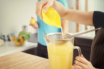 Woman pouring freshly squeezed lemon juice into glass jug on table