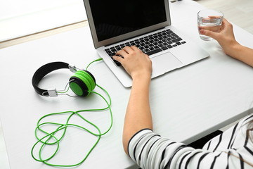 Woman using laptop with connected headphones on table