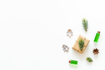 Composition with New Year gift wrapped in craft paper and decorted with pine sprout near pine sprigs, cones, spruce figure, fir oil on white background top view copy space