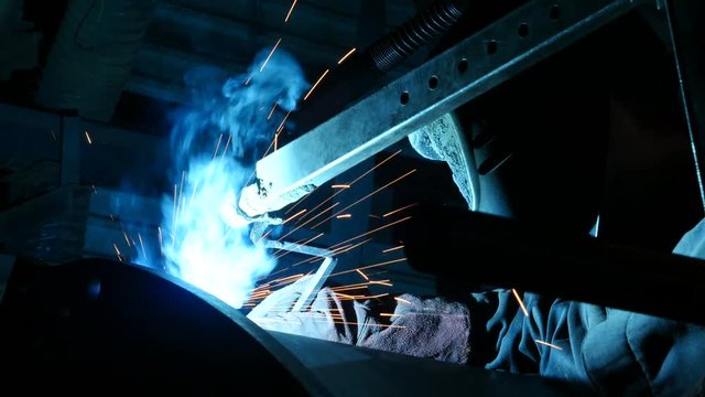 Plant worker welding metal in dark