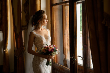 Wedding. Portrait of beautiful bride in luxury wedding dress posing near window