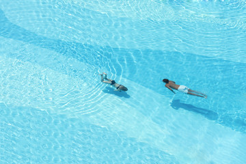 Aerial top view on the men and woman in the swimming pool with transparent blue water. in motion