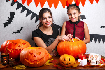 Fototapeta premium Happy Halloween! Mother and daughter carving pumpkin. Family preparing for holiday.
