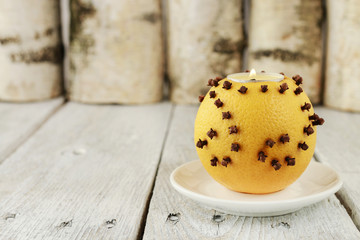 Orange pomander ball with candle on wooden table.