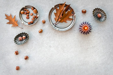 Obraz premium Autumn composition with candlelight and hazelnuts on rustic metal trays.