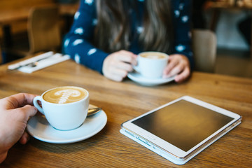 People enjoy their morning coffee in a cafe and communicate with each other. The tablet is on the table.