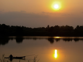 Beautiful yellow sunset over the river and pond with trees and forest in silhouette background.