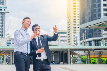 Two business people with coffee chatting and pointing up while showing office to colleague in the morning at outdoor covered walkway